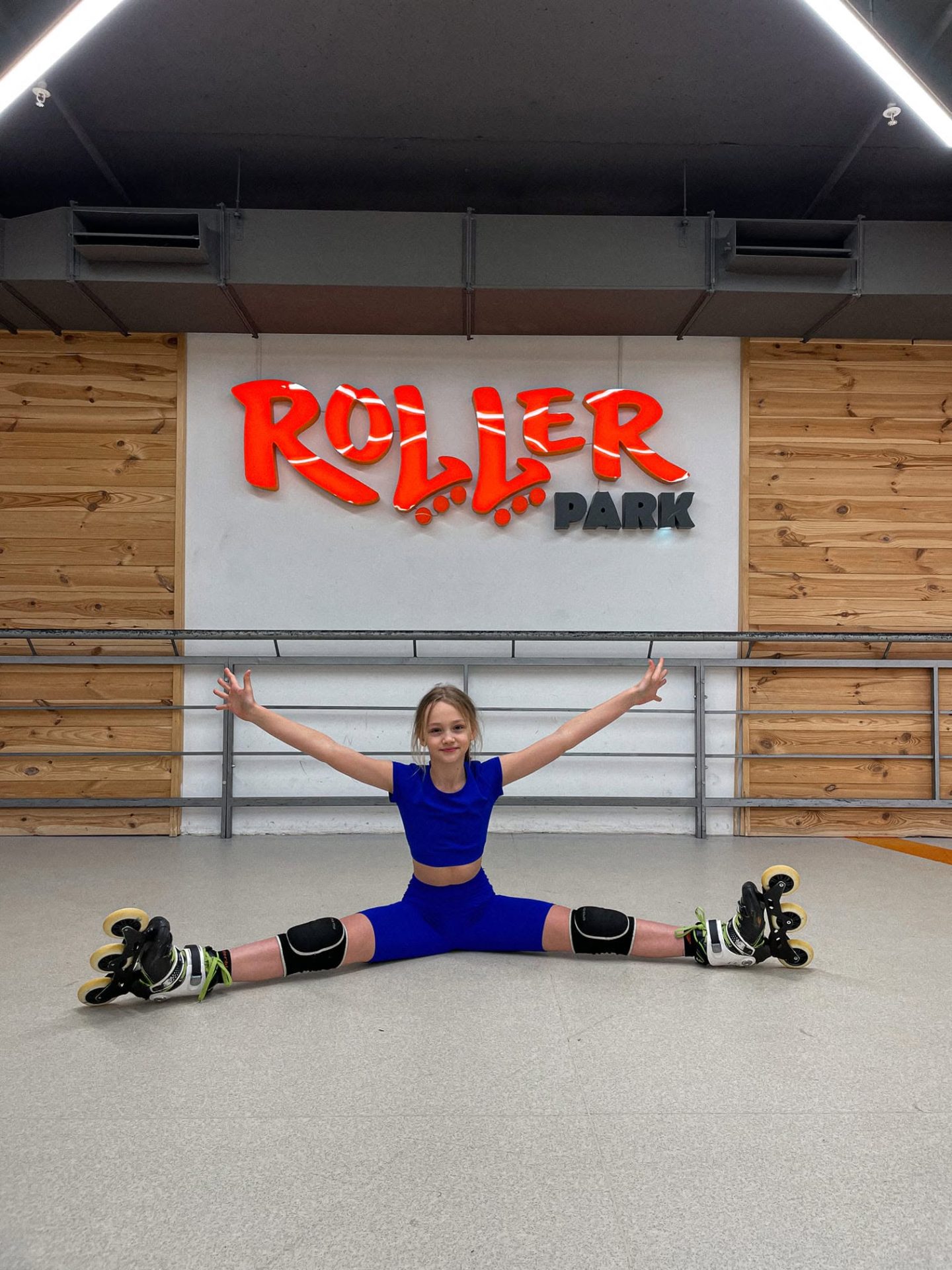 Tânără patinatoare executând șpagatul pe role sub sigla Roller Park